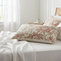 Cream and blush pink floral farmhouse decorative pillow on white linen bed